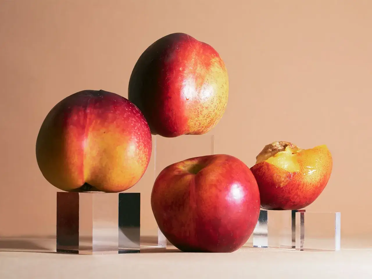 Drei ganze und eine angeschnittene Nektarine auf Glaspodesten. Die Früchte sind rot und gelb gefärbt, ideal zum Lagern.