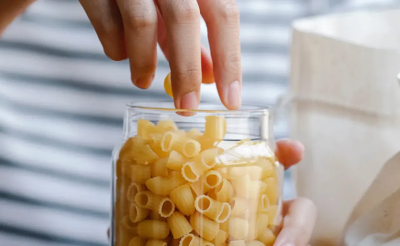Hände legen gekochte Nudeln in ein Glas, um sie aufzubewahren.