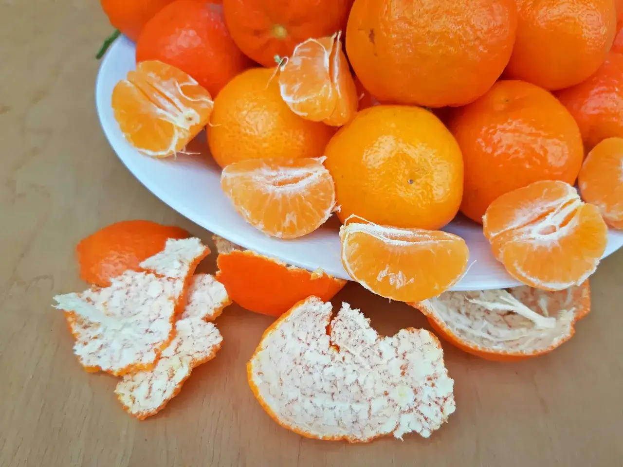 Ein Teller voller saftiger Mandarinen, einige geschält und in Spalten geteilt, daneben die orangen Schalen. Perfekt zum Lagern und Genießen.